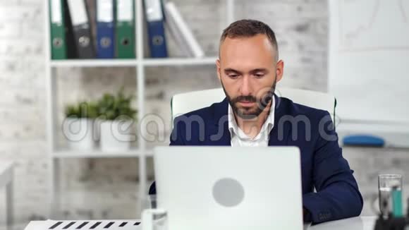 自信时尚的男老板穿着西装专注地看着在现代办公室工作的屏幕笔记本电脑视频的预览图