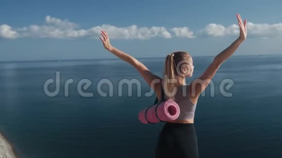 从侧面看身穿运动服的女人站在悬崖边上张开双臂视频的预览图