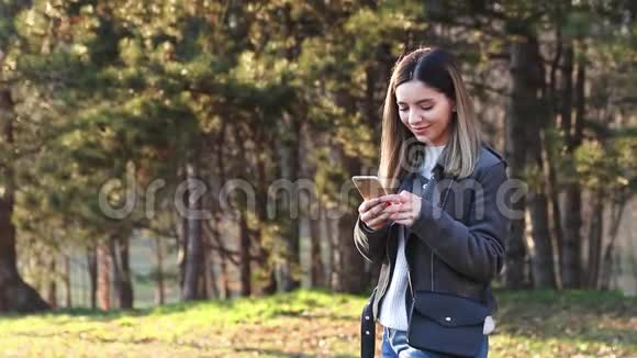 春天日落时分在公园里用手机观看欢快的美丽女子视频的预览图