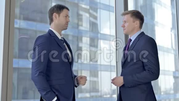 两位中年商人在会议室办公室的窗户上交谈视频的预览图