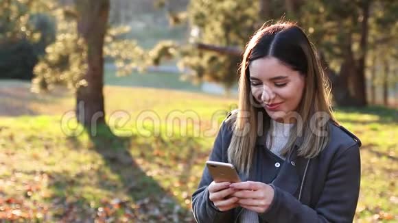 春天日落时分在公园里用手机观看欢快的美丽女子视频的预览图