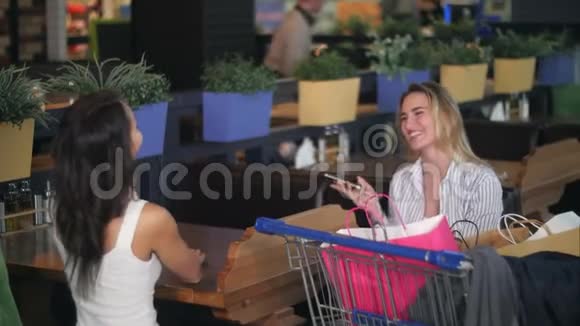 朋友们在购物后在商场的一家咖啡馆休息和使用智能手机视频的预览图