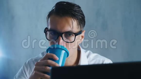 在办公室工作的戴眼镜的年轻人用电脑做特写商人喝咖啡或茶在视频的预览图