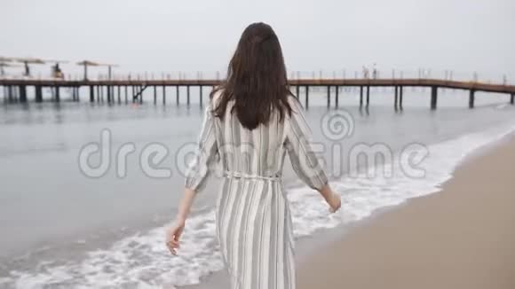 快乐的女人穿着一件长裙子光着脚在海滨散步笑着享受生活视频的预览图