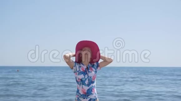 孤独优雅的女人穿着蓝色的泳衣粉红色的帽子站在海边看着地平线视频的预览图