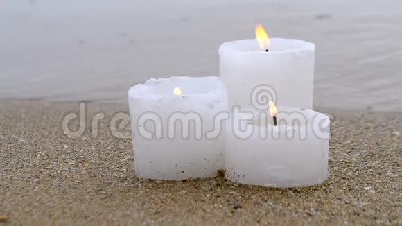 三支黄色的小蜡烛靠近蓝色海洋海浪的沙滩视频的预览图