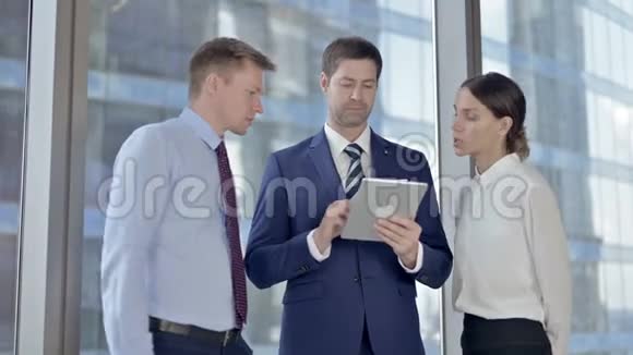 中年商人和他的助手们在平板电脑上滚动着视频的预览图