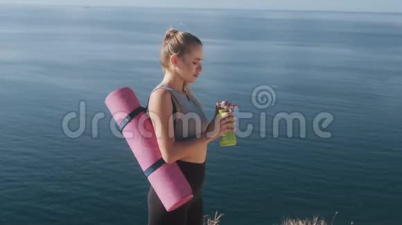运动服的女士在海边运动后从瓶子里喝水视频的预览图