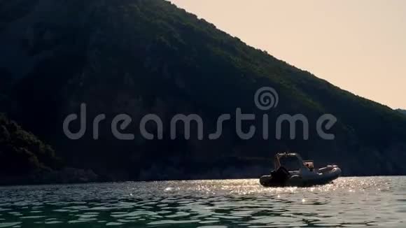 湾在山脚下太阳阳光反射在爱琴海的海水中在柔和的波浪中在日落时停泊的船视频的预览图