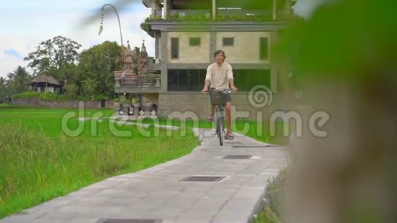 一个年轻人骑着自行车穿过美丽的稻田前往东南亚的概念慢镜头视频的预览图