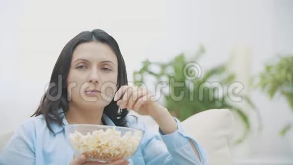 慢点一个可爱的女人一边吃着爆米花一边惊讶地看电视好吃好吃4K视频的预览图