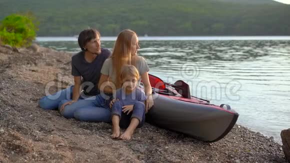 一个年轻的家庭父亲母亲和儿子坐在湖边或海滨的充气皮艇旁慢镜头视频的预览图