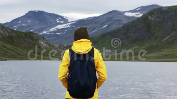 穿着一件亮黄色夹克的女子背包客站在一个山湖前视频的预览图