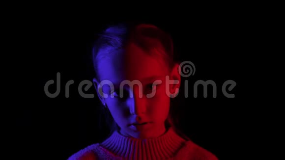 年轻女孩仰望黑色背景在黑暗的工作室与蓝色和红色照明肖像少女摆在面前视频的预览图