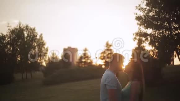 爱的一对情侣在夕阳下在阳光下接吻两个情人在公园日落时接吻的剪影视频的预览图