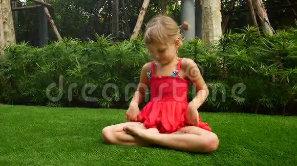 小女孩正以莲花的姿势坐在草地上女孩冥想和唱歌视频的预览图