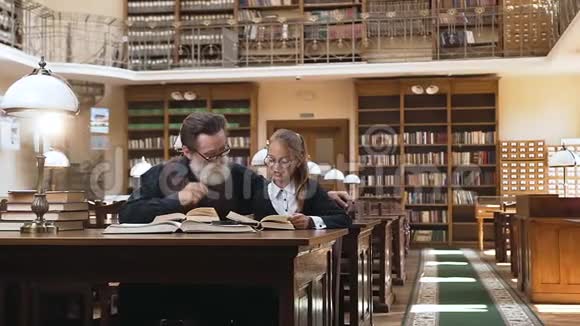 聚精会神的长胡子老人戴着眼镜坐在图书馆的桌子旁听着他那可爱的少年怎么读视频的预览图