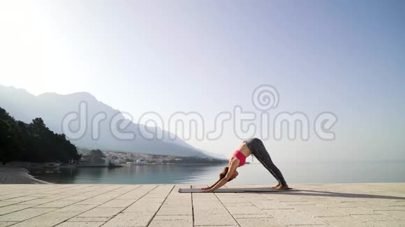 运动女子在海滨木板路上做瑜伽背景是山视频的预览图