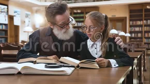 坐在图书馆看书的令人愉快的祖父和孙女的精彩画像视频的预览图