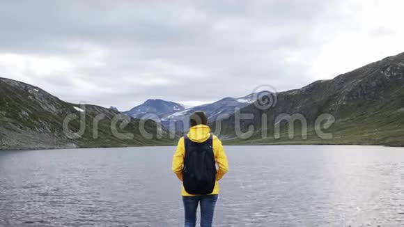 穿着一件亮黄色夹克的女子背包客站在一个山湖前视频的预览图
