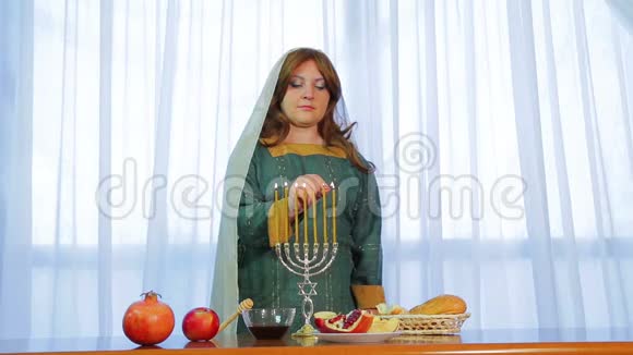 在节日聚会上一位犹太妇女在RoshHashanah的一个漂亮的烛台上点燃蜡烛并提供款待视频的预览图