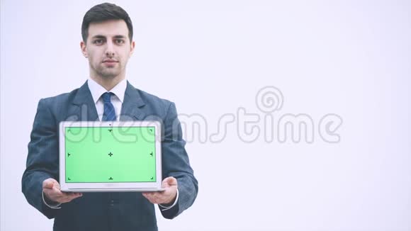 英俊的商人穿着灰色西装打着领带站着拿着一台带绿色屏幕的笔记本电脑点头显示出视频的预览图