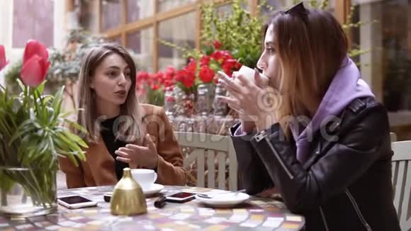 两个女人在咖啡厅一起喝咖啡他们坐在咖啡店的桌子旁聊天动作缓慢人民视频的预览图