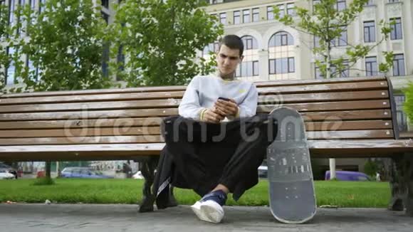 帅哥坐在公园的长凳上用手机听音乐拐杖和滑板就在附近视频的预览图