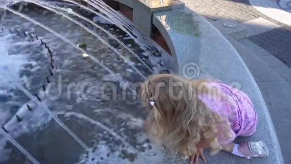 穿裙子的金发小女孩在夏天玩喷泉水手持射击视频的预览图