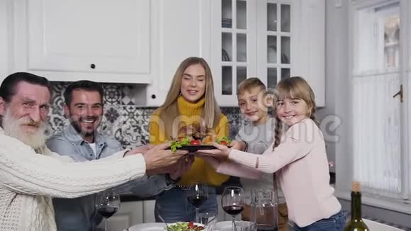 可爱的微笑的父母孩子和爷爷手里拿着烤火鸡在感恩节看着镜头视频的预览图