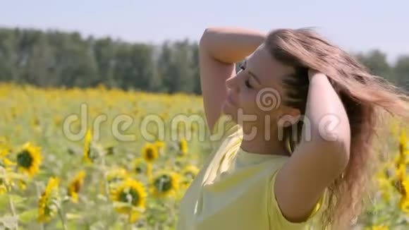 一位留着长发的美丽女子站在一片向日葵的田野里放松头发在风中撕裂视频的预览图