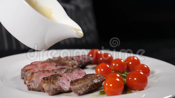 厨师在餐厅做饭厨师在烤肉片上撒上一些白酱在白色盘子上配上樱桃番茄视频的预览图