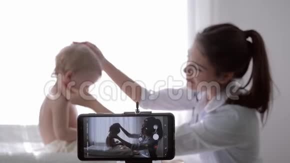 博客流行的vlogger女医生在婴儿体检期间为智能手机上的vlog拍摄新一集视频的预览图