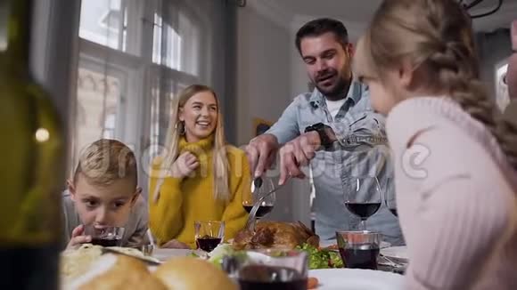 幸福快乐的一家人坐在宴会桌旁看着微笑迷人的父亲切烤火鸡视频的预览图