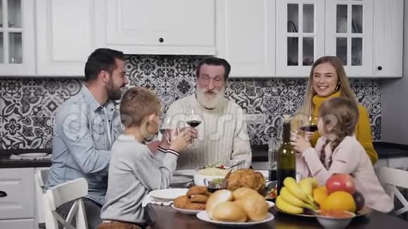 漂亮的幸福家庭坐在节日的餐桌上吃着美味的饭菜手里拿着酒杯和葡萄酒视频的预览图