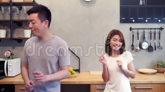 美丽快乐的亚洲夫妇正在家里的厨房里跳舞年轻的亚洲夫妇有浪漫的时间在家听音乐视频的预览图