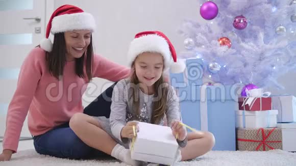 在新年的时候妈妈和女儿围着礼物坐在圣诞树附近的地毯上视频的预览图