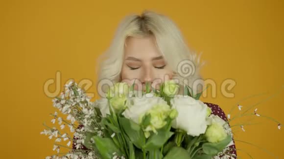 幸福的金发女孩用闭着眼睛嗅花的正面景色视频的预览图