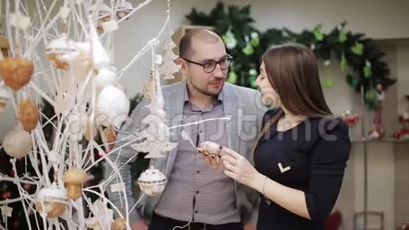 这对相爱的夫妇在超市挑选圣诞装饰品一个女人在考虑圣诞舞会视频的预览图
