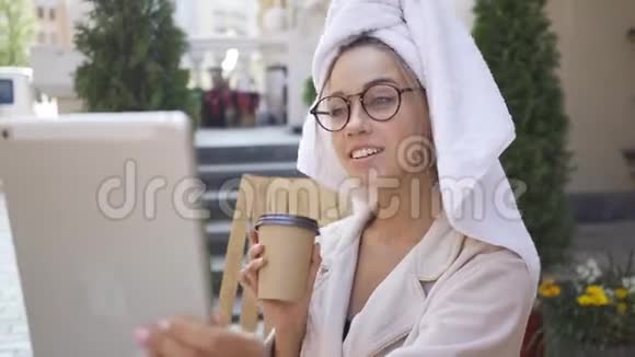 戴着眼镜和浴袍头上戴着毛巾头上戴着毛巾看着坐在后院的平板电脑自信视频的预览图