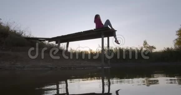一个女人坐在木墩上的肖像看着湖感觉自由概念自由美丽的湖景视频的预览图