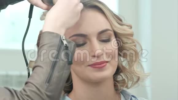 年轻漂亮的女人在美容院使用智能手机而理发师则做发型视频的预览图