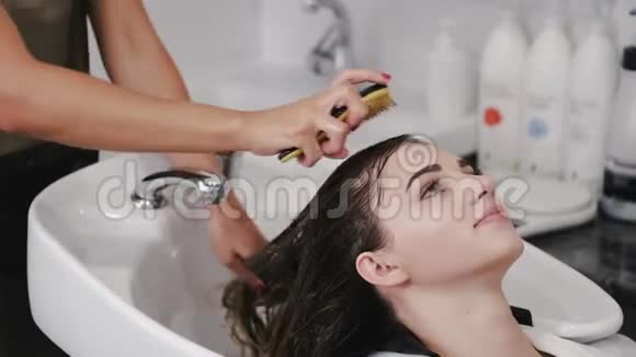 理发师洗头发的女人她的头发用白色水槽洗发水视频的预览图