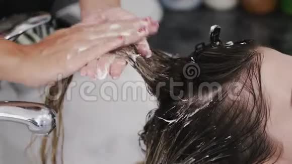 理发师用白色水槽洗洗发水的女人的头发视频的预览图