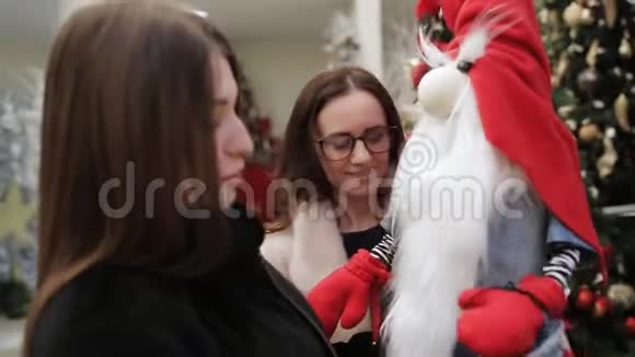 两个女人带着微笑和兴趣在一个新年超市里的圣诞侏儒的身影视频的预览图