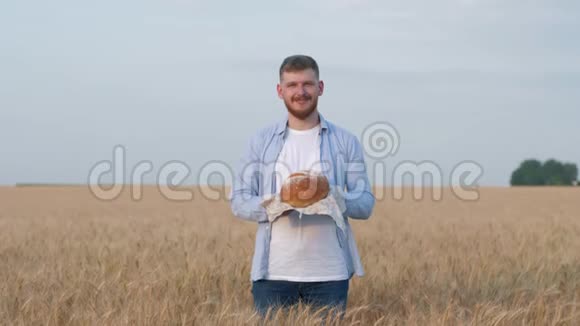 收获年轻的农学家快乐的人给你新鲜烘焙的面包微笑着站在成熟的谷物镜头视频的预览图