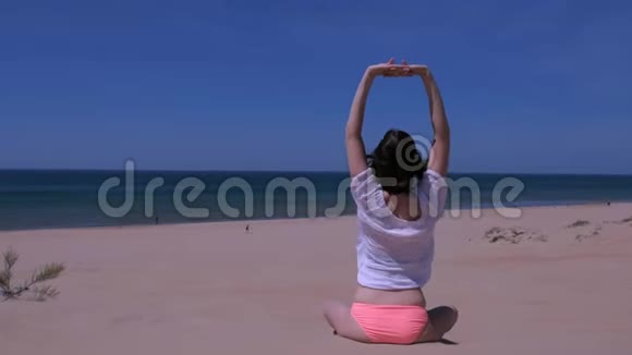 女子伸展瑜伽练习坐莲姿沙海沙滩双手仰视视频的预览图