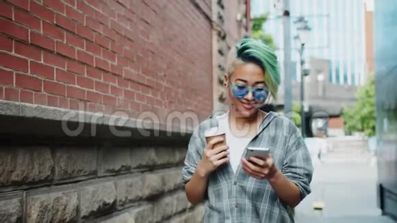 带着咖啡和智能手机走在户外的漂亮亚洲女人的慢动作视频的预览图