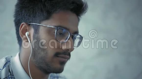 特写镜头带眼镜和耳机的印度男人喝咖啡看笔记本电脑显示器视频的预览图
