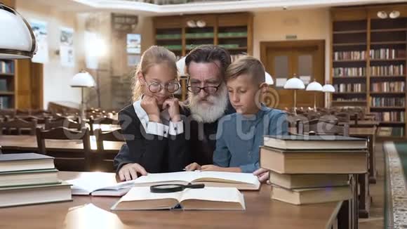 有经验的老人和他的孙子们坐在图书馆看书的美丽画面视频的预览图